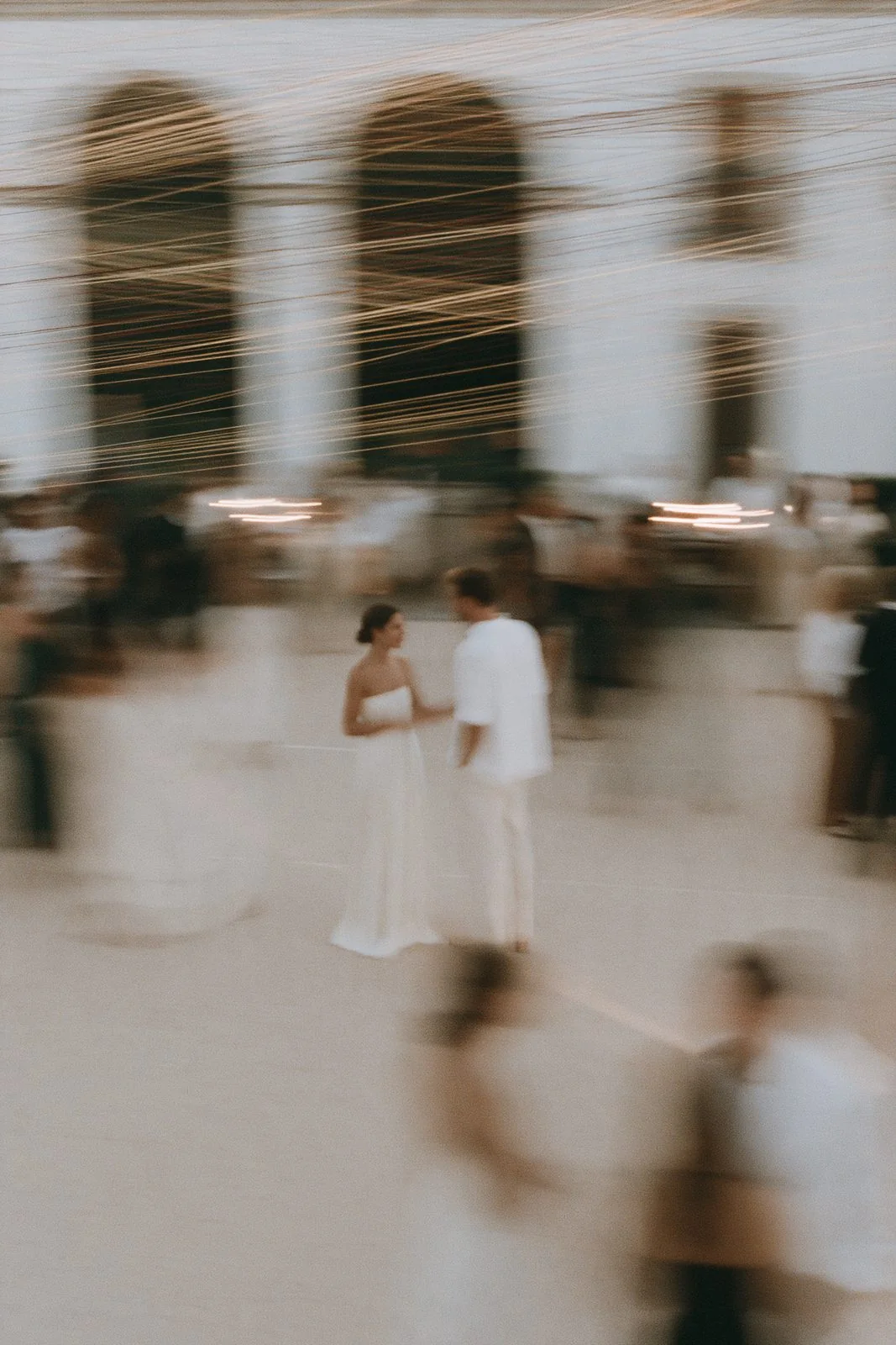 A couple in white meeting in a pale hall as the room moves around them